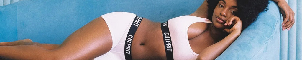 Woman lying on a blue couch wearing white underwear with 'Culprit' branding on the waistband.